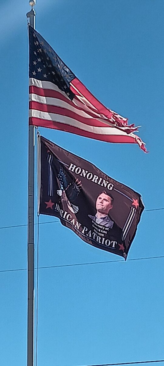 American flag flying alongside a tribute flag that reads "Honoring American Patriot," featuring a portrait and eagle design. This affordable and high-quality flag is perfect for showing patriotism. Buy online now at UltimateFlags.com.