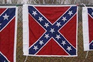Confederate flag displayed on a fence, showcasing vibrant red and blue colors with white stars. Perfect for collectors or those seeking a statement piece, this flag is available at a cheap and affordable price. Buy online for the best deals at UltimateFlags.com.